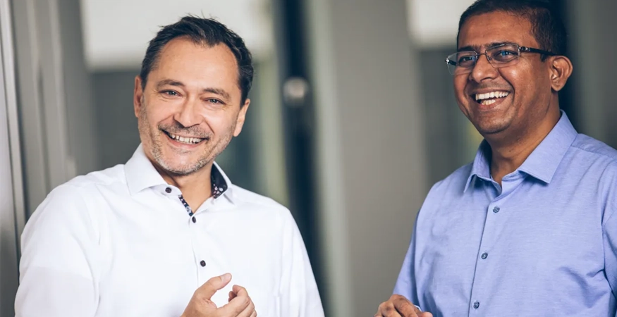 Edward Aston und ein Kollege lächen in die Kamera. 