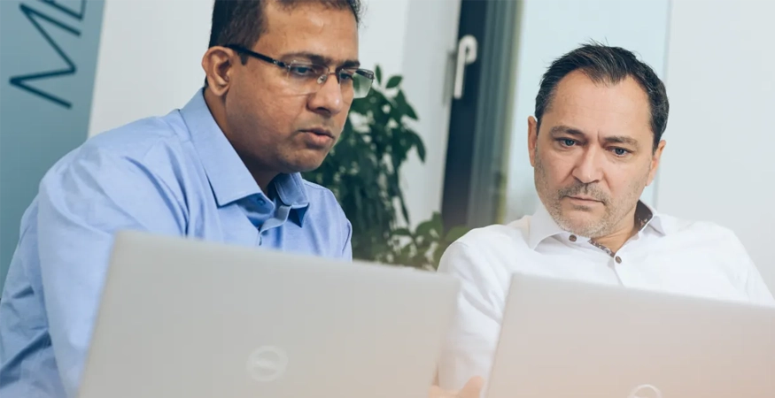 Edward Aston und ein Kollege sitzen konsentriert vor Laptops. 