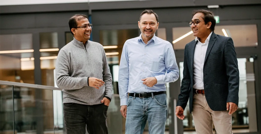 Edward Aston und zwei Kollegen stehen in einem Gebäude und lächeln. 