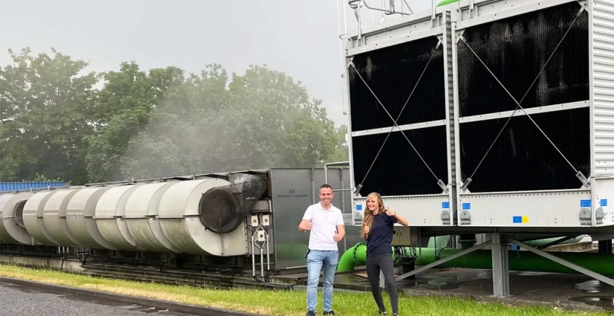 Zwei Personen posen vor einer Anlage und zeigen mit dem Daumen nach oben.