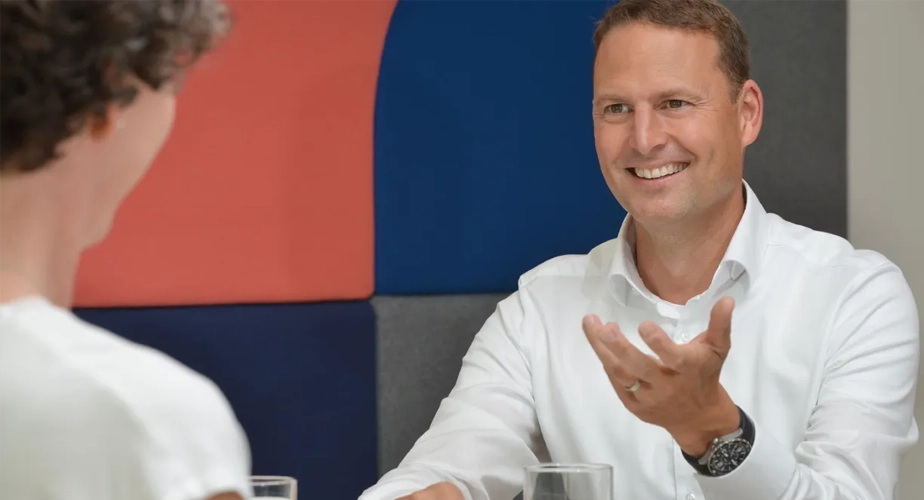 Zwei Personen reden mit einander, eine Person lächtelt und gestukuliert mit den Händen. 